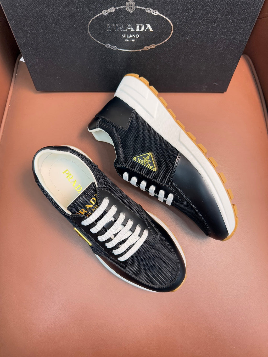 Prada unisex sneakers side view, dark upper, white laces, tan gum outsole.