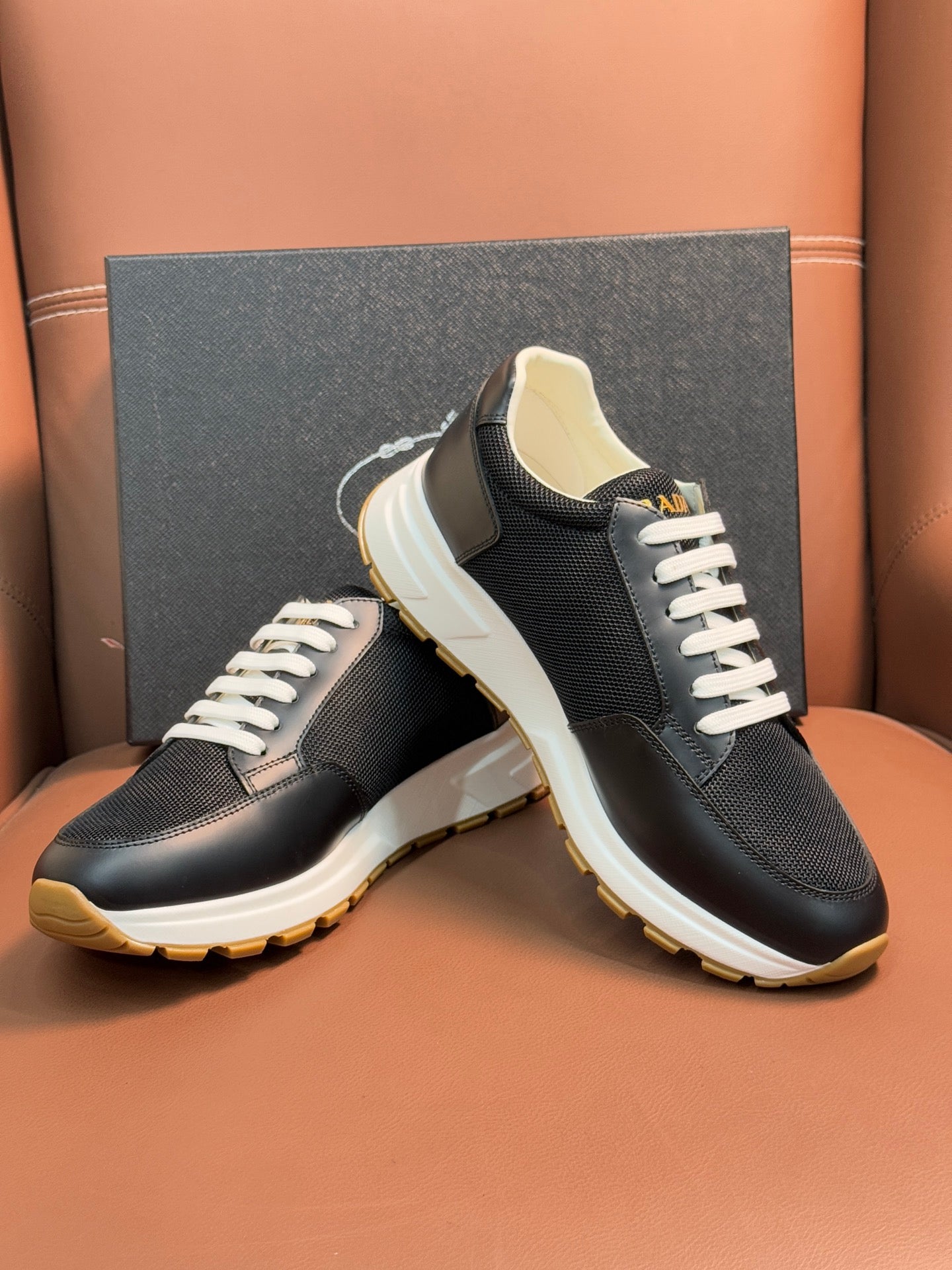 Prada unisex sneakers angled pair, dark uppers, white laces, thick white sole.