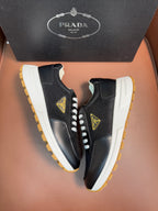 Prada unisex sneakers with side logo patch, dark upper, white laces, yellow-edged sole.
