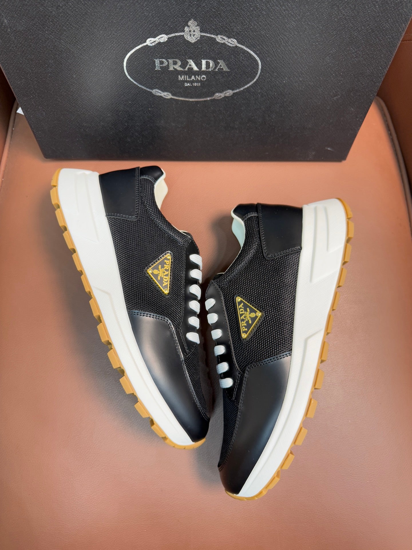 Prada unisex sneakers with side logo patch, dark upper, white laces, yellow-edged sole.