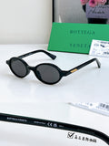 Bottega Veneta oval sunglasses with black frames and dark lenses, gold temple accents.