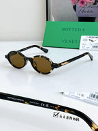 Bottega Veneta oval sunglasses with dark frames and amber lenses, gold temple detail.
