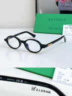 Bottega Veneta oval sunglasses with dark frames and blue-tinted lenses, gold temple accent.