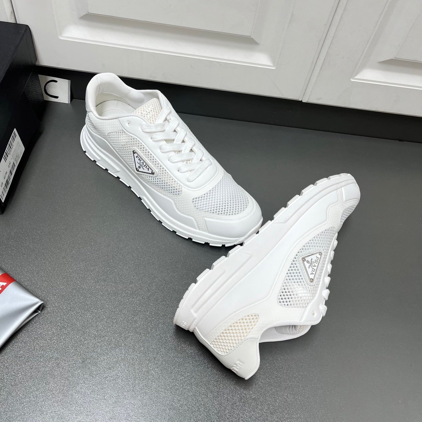 White Prada sneakers, side and heel angle, with mesh uppers and rubber tread