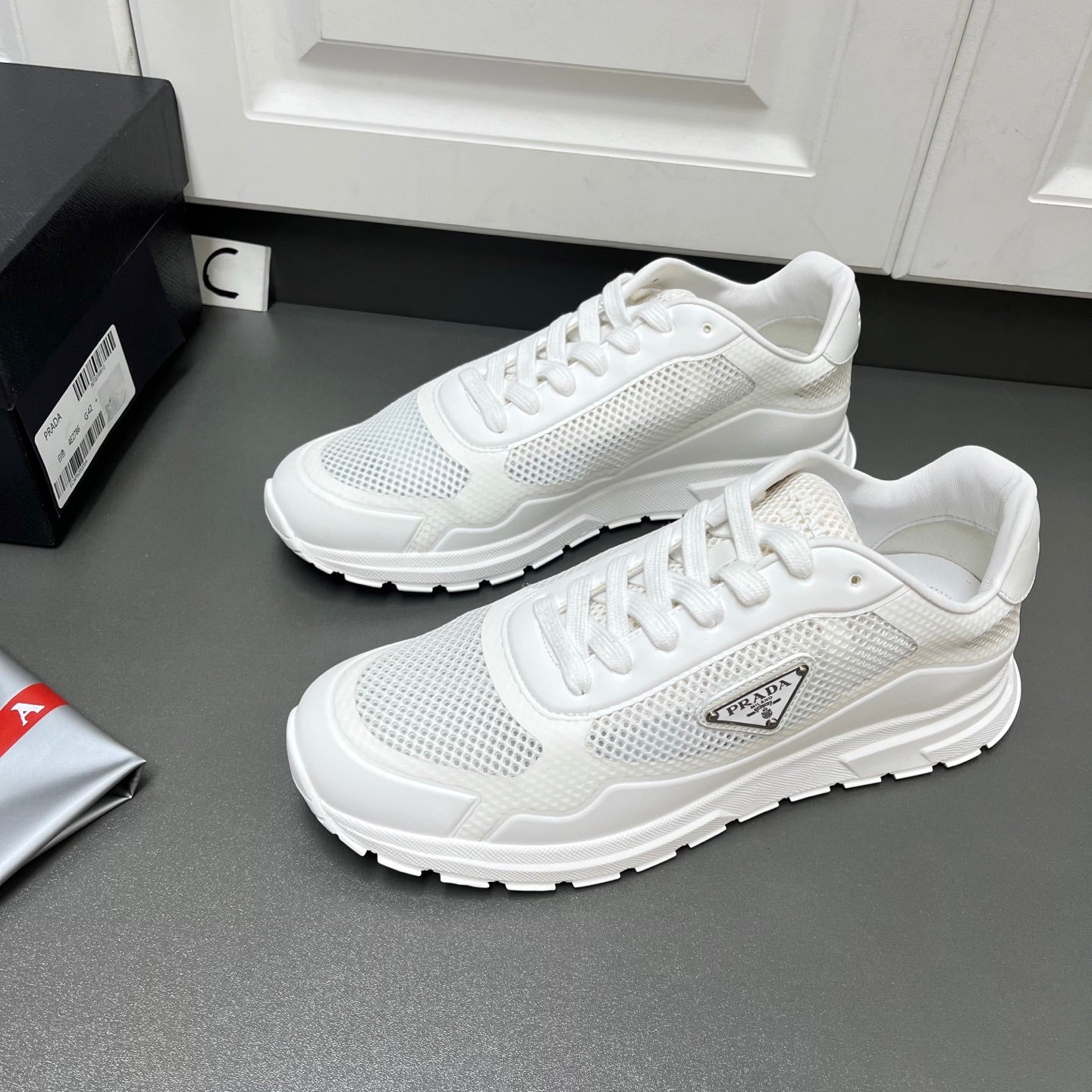 White Prada sneakers showing lace-up mesh upper and textured side logo patch