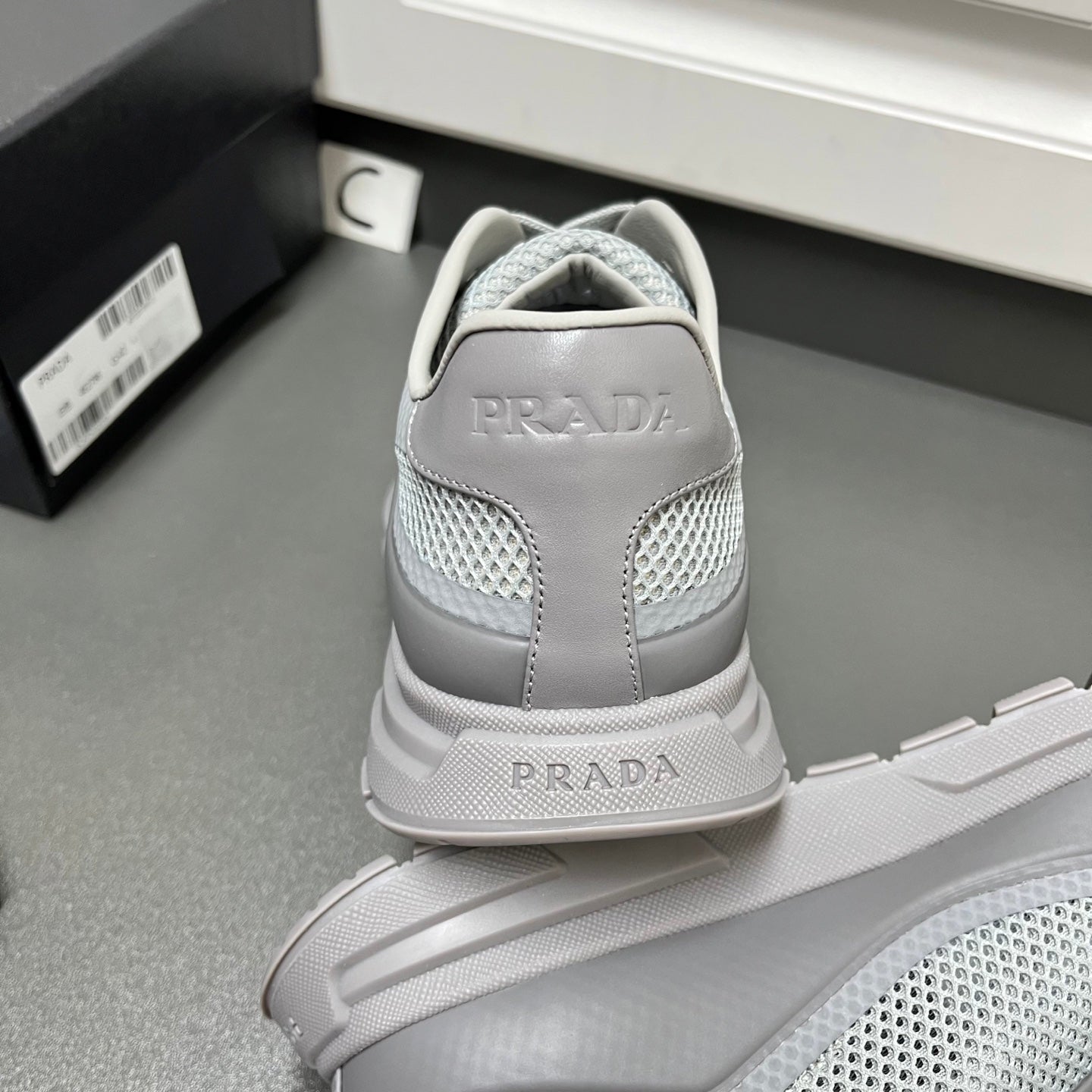 Prada unisex sneakers back view, light gray with PRADA on heel and molded sole