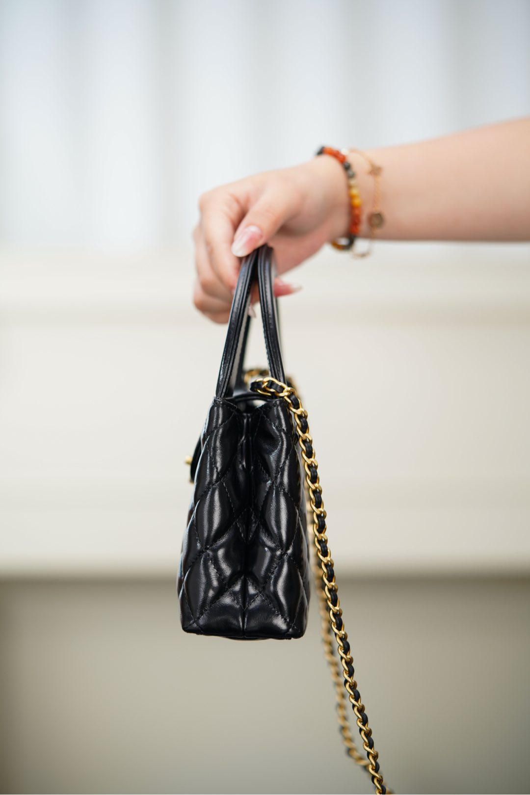 Black Chanel quilted mini handbag side view with gold chain shoulder strap