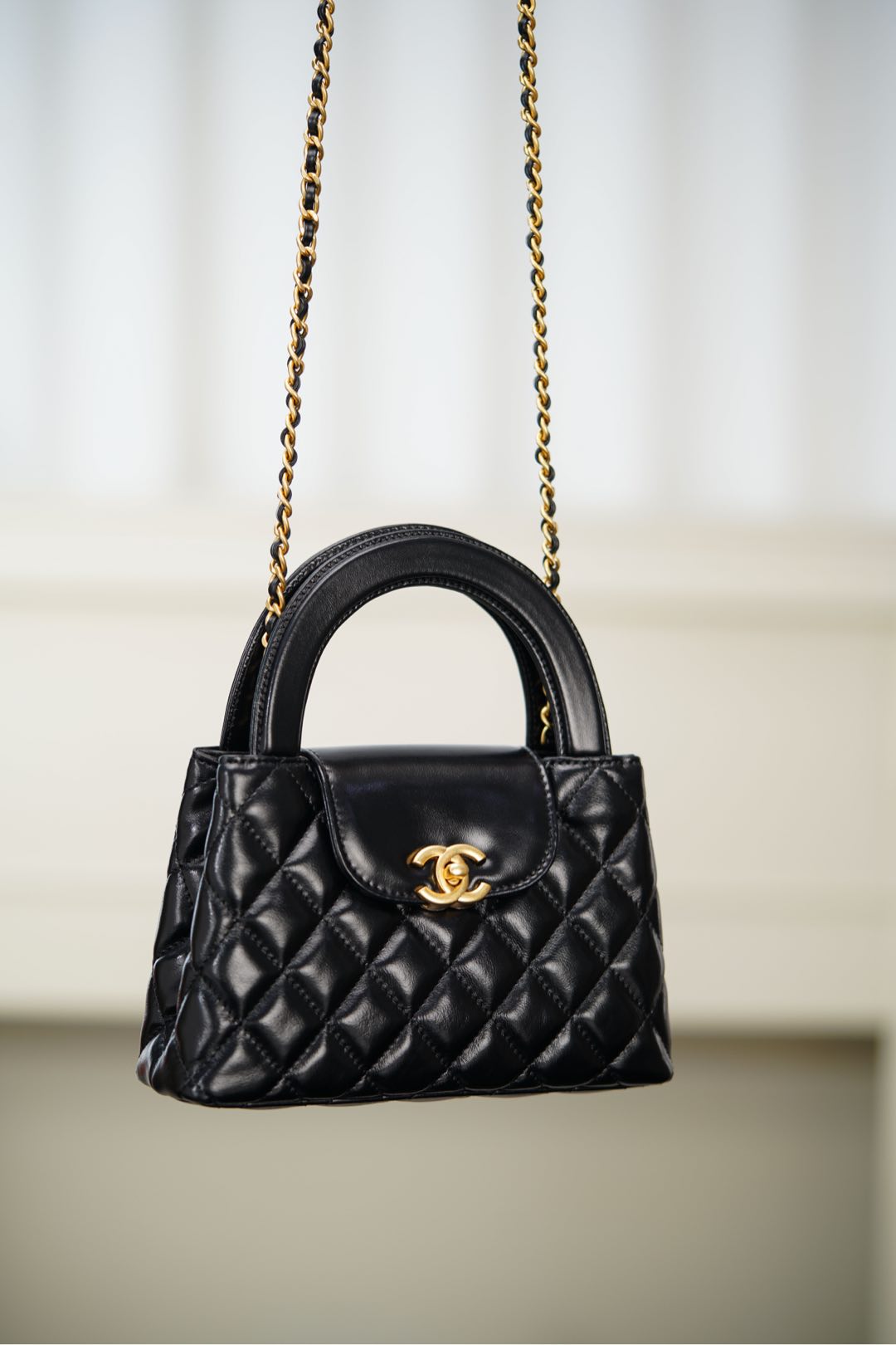 Black Chanel quilted mini handbag with top handle and gold chain shoulder strap