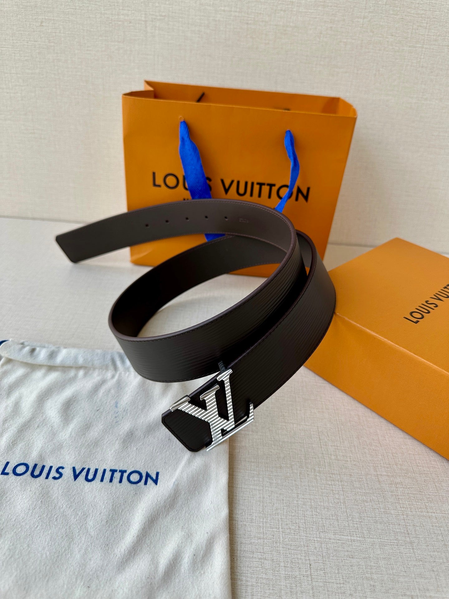 Louis Vuitton belt with black textured strap and LV buckle, stacked view.