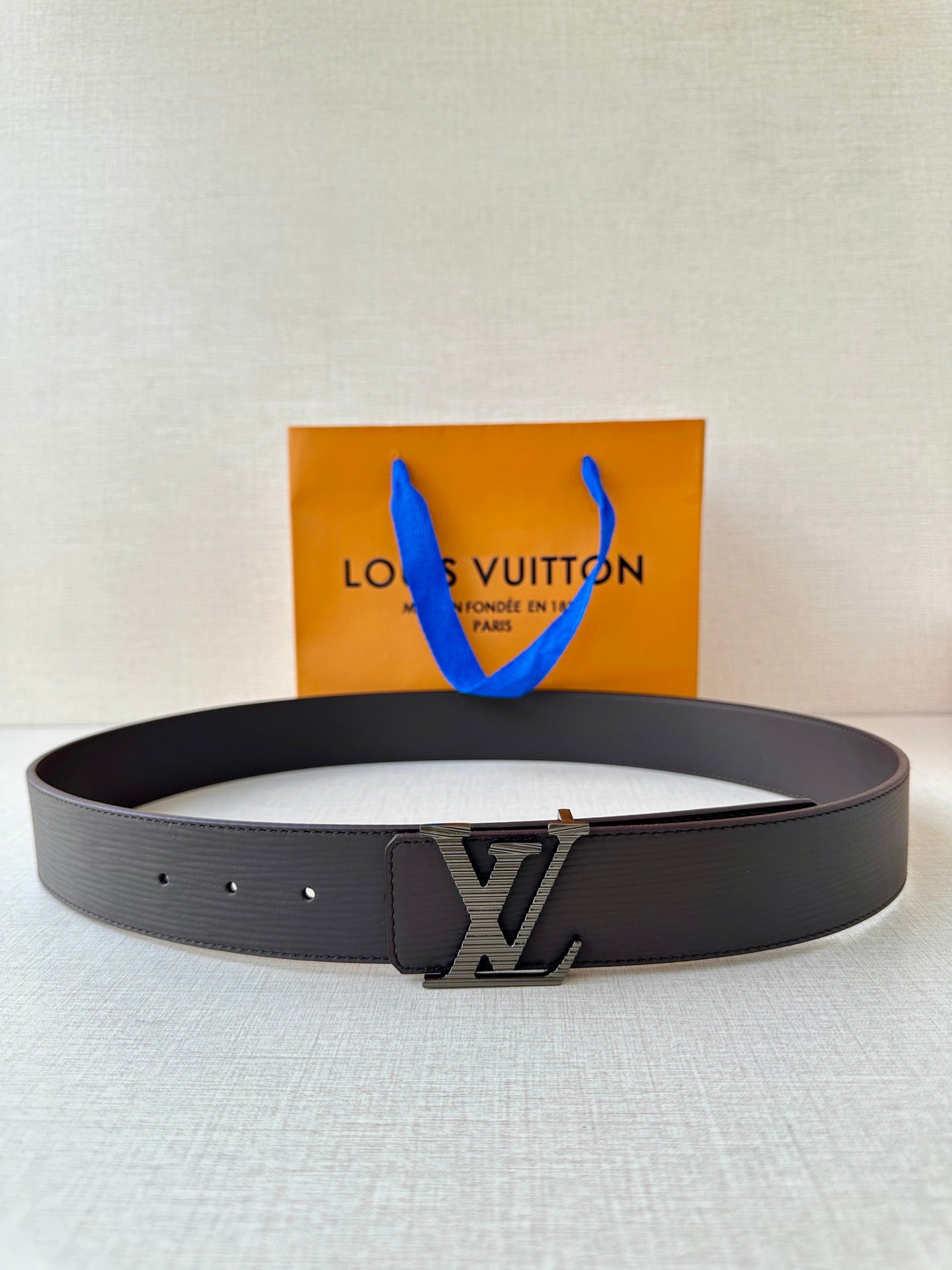 Louis Vuitton belt with dark textured strap and LV logo buckle, laid flat.