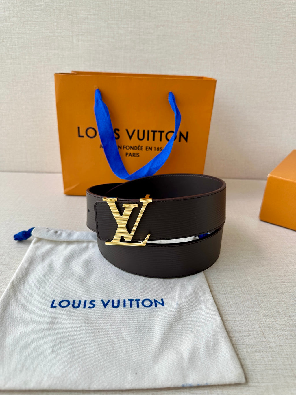 Louis Vuitton belt with black strap and LV logo buckle, upright on fabric.