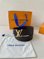 Louis Vuitton belt with black strap and LV logo buckle, upright on fabric.