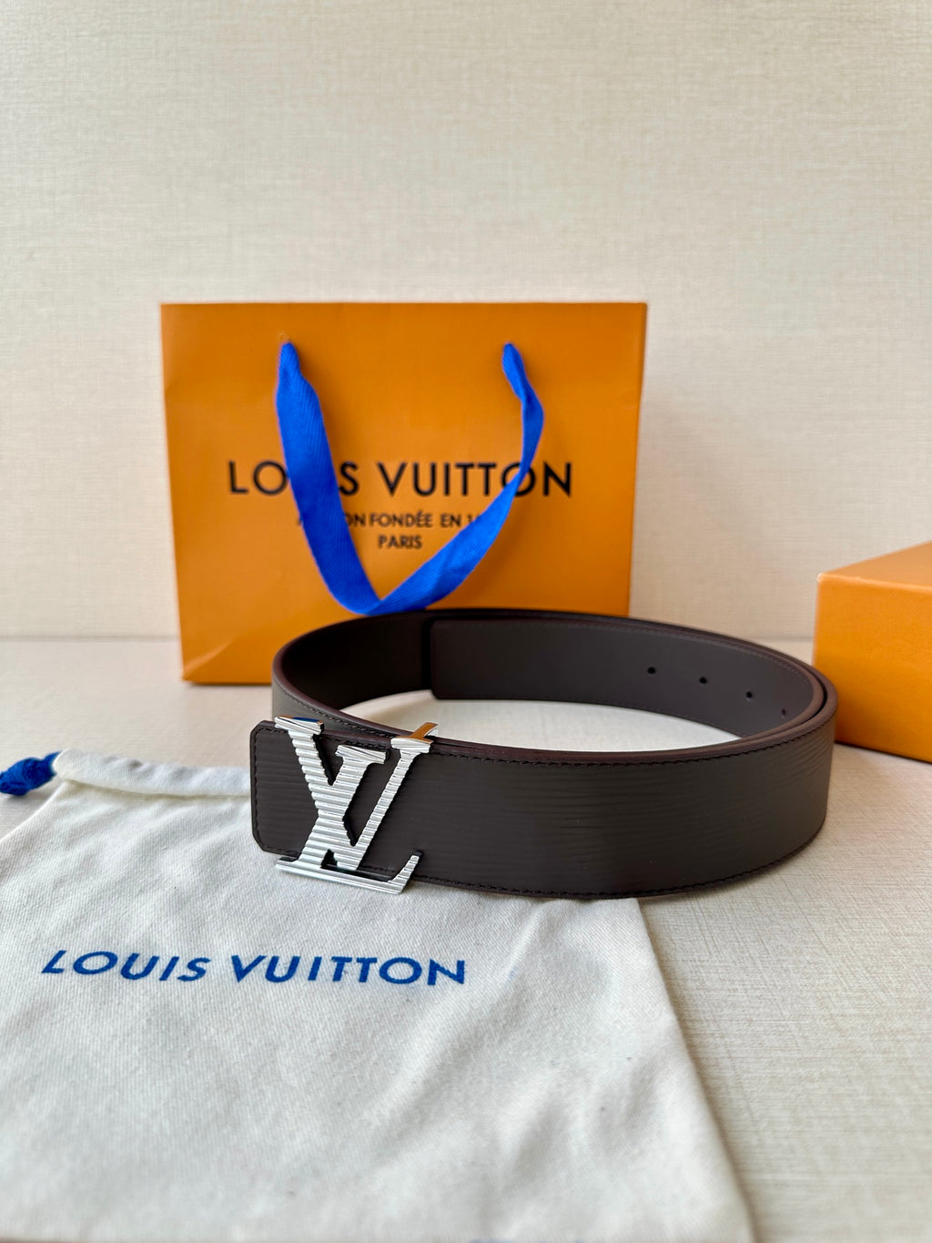Louis Vuitton belt with dark strap and LV logo buckle, styled on cloth.