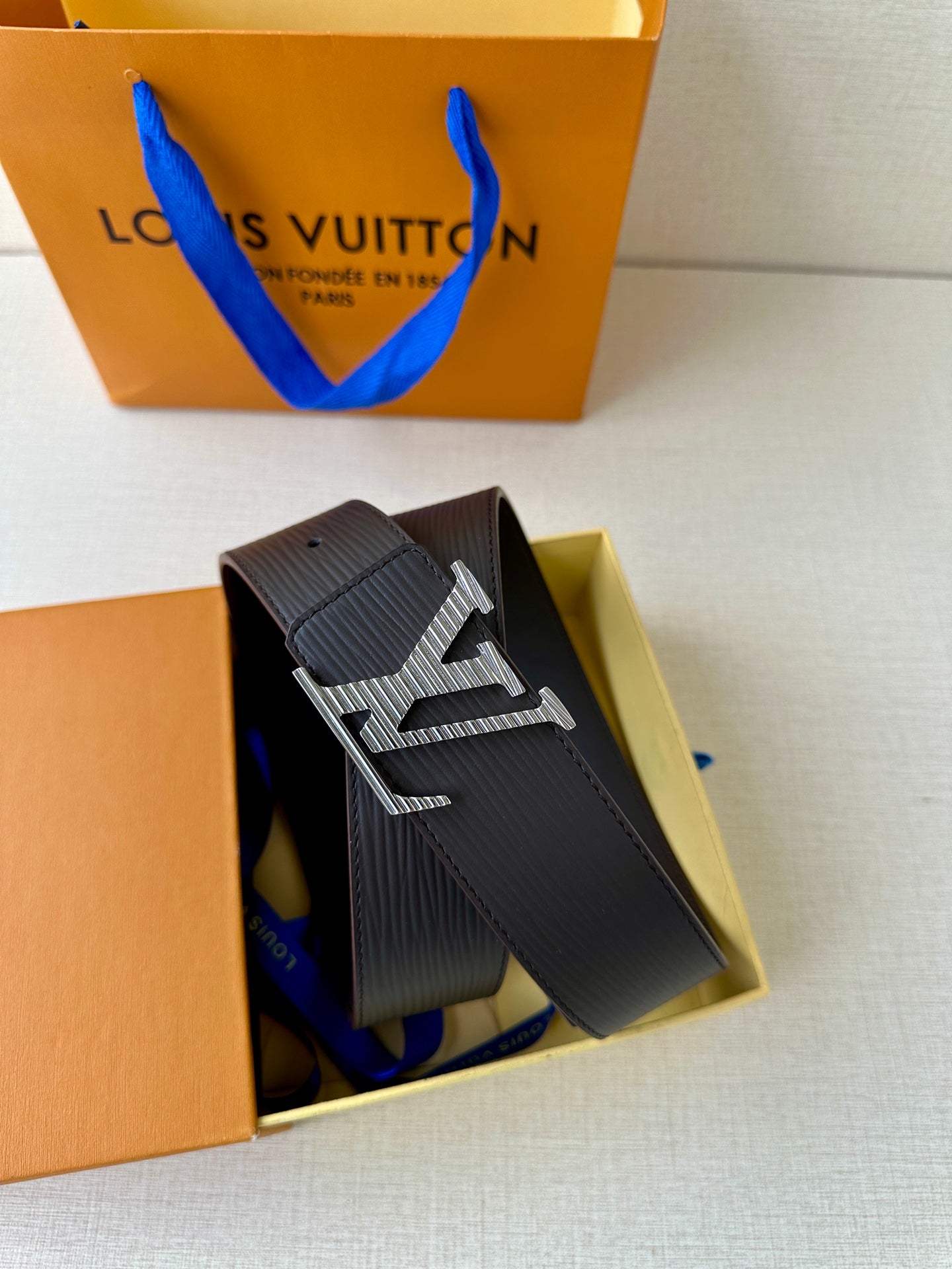 Louis Vuitton belt with dark textured strap and LV buckle inside a box.