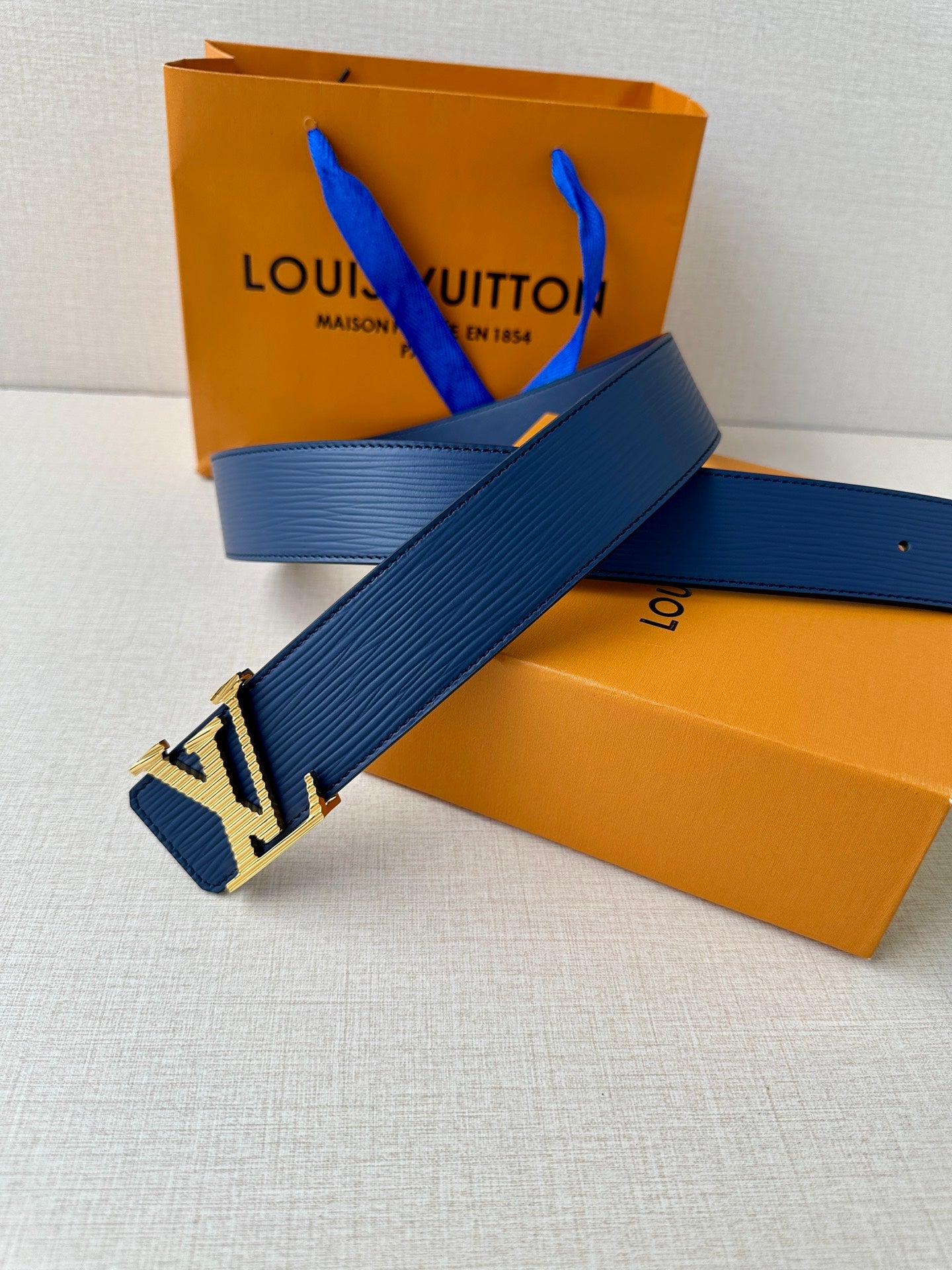 Blue leather Louis Vuitton belt with gold-tone LV buckle laid across a surface