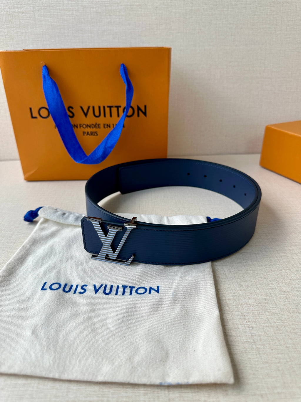 Blue leather belt with gold-tone LV buckle, resting on a fabric pouch