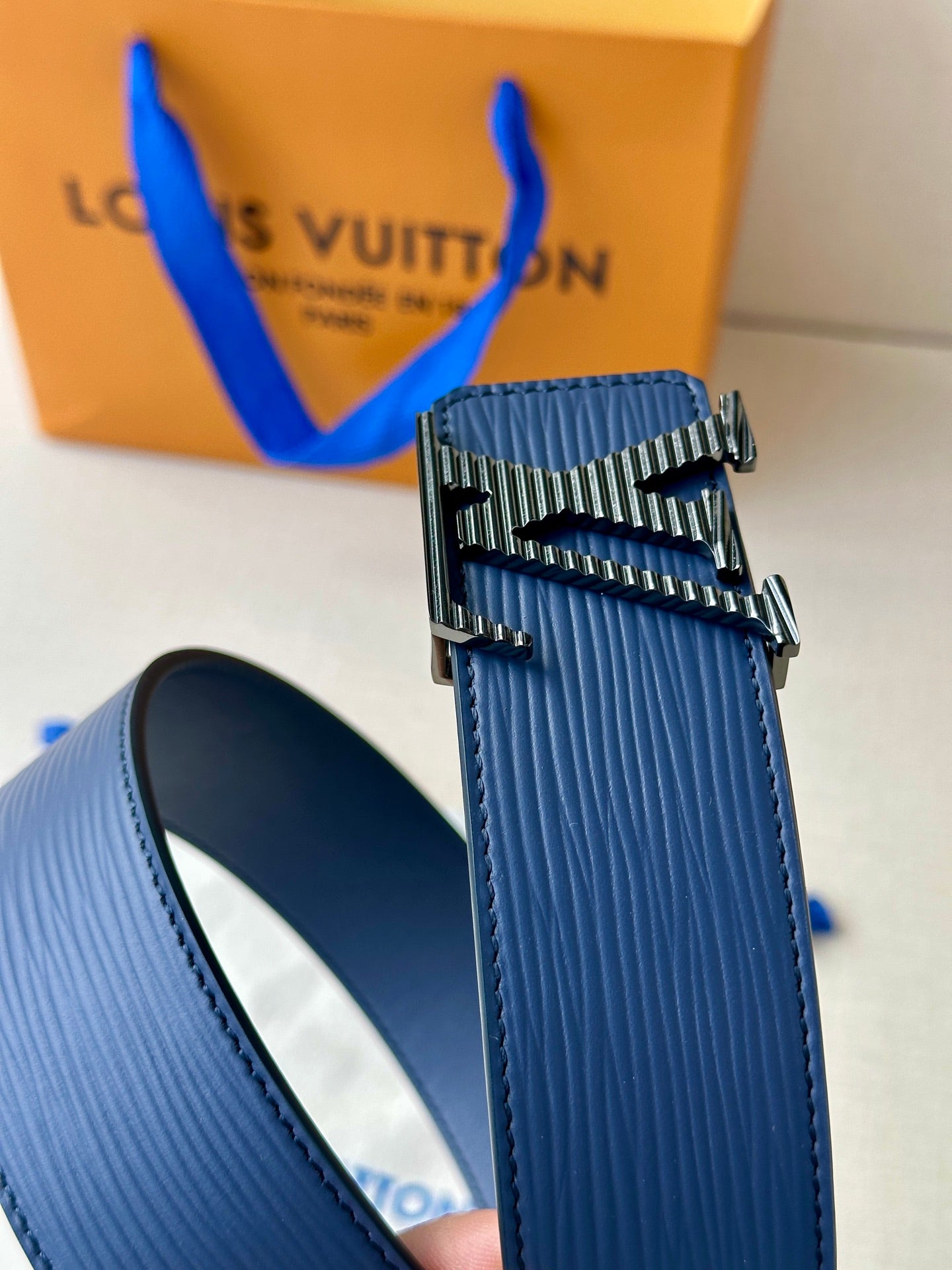 Blue leather belt with silver-tone and gold-tone LV buckle; side view