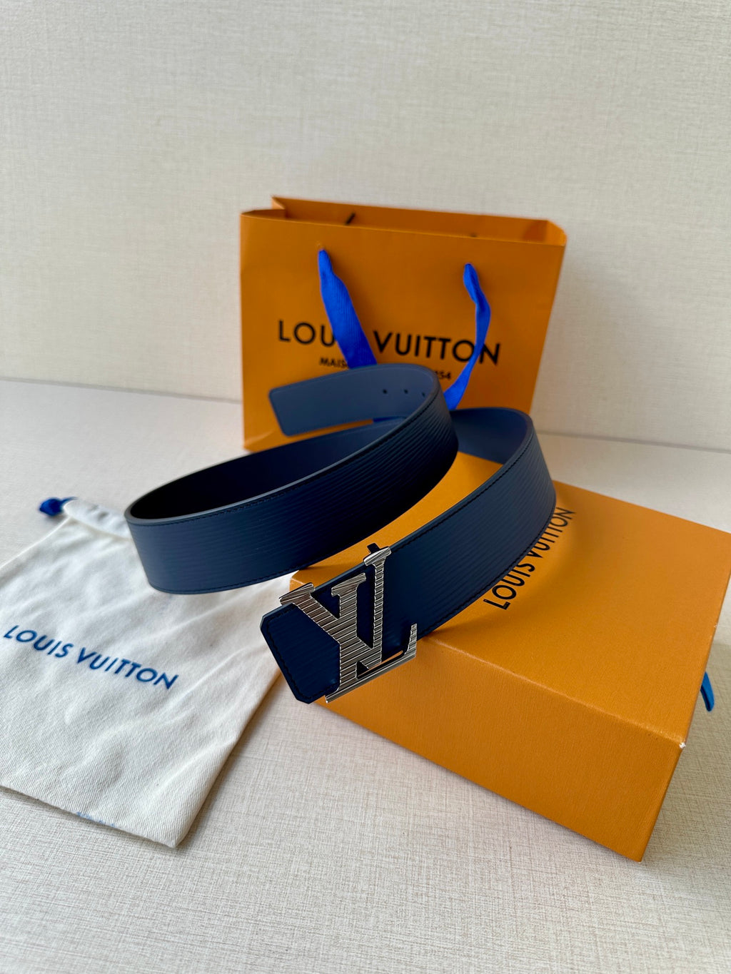 Blue leather belt with gold-tone LV buckle on top of a fabric pouch
