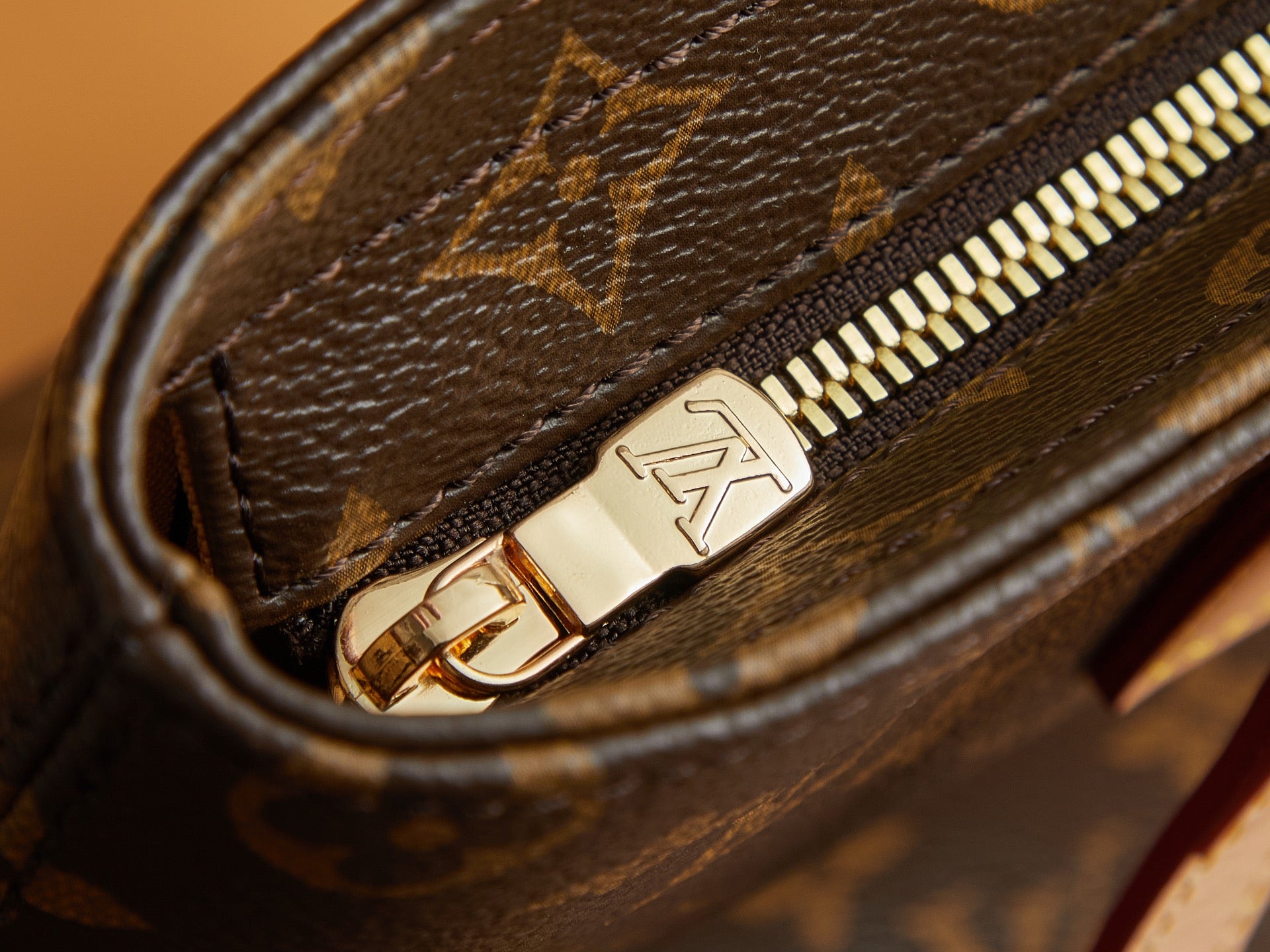 Louis Vuitton monogram zipper pull on brown canvas with gold hardware.