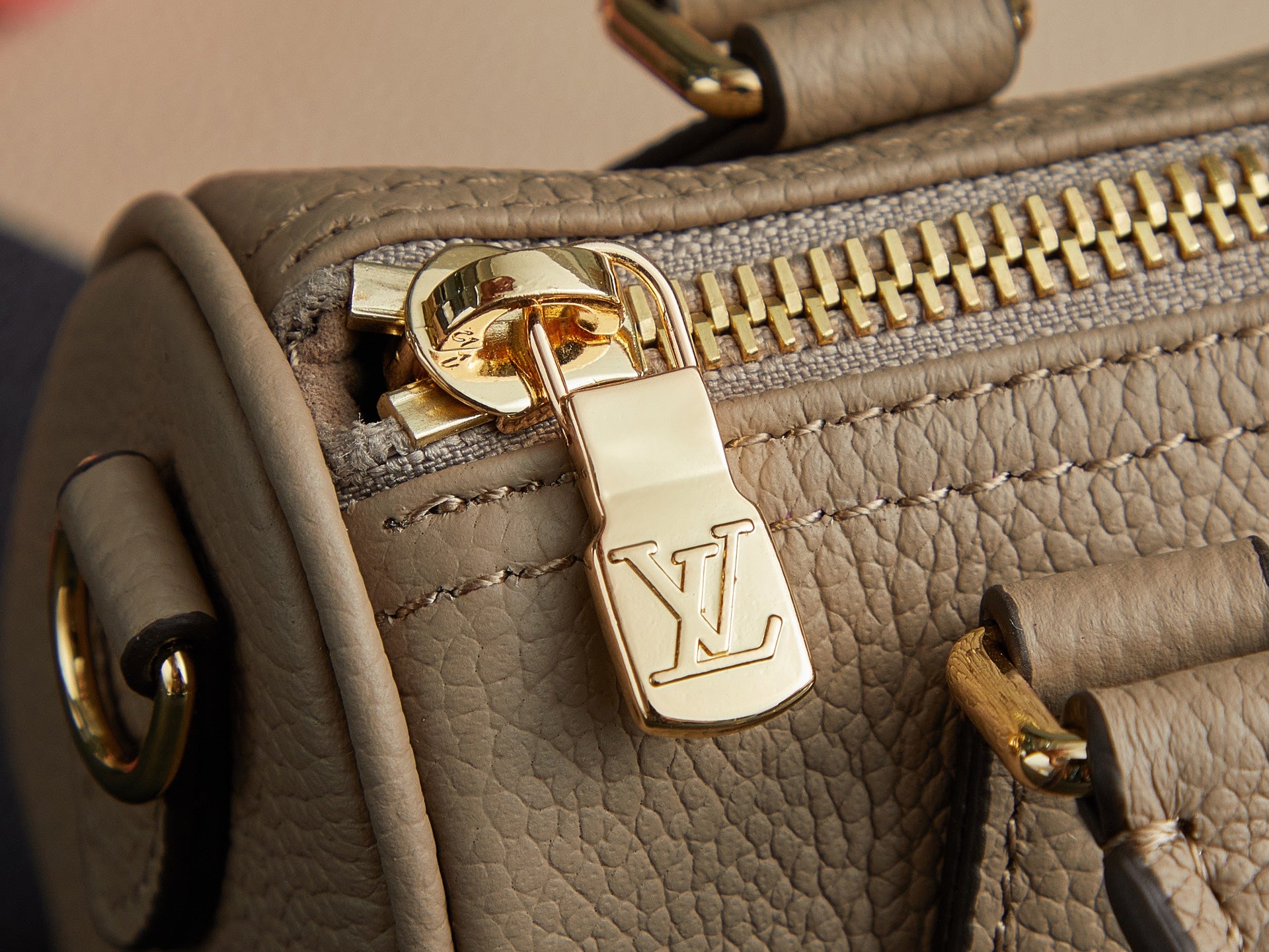 Louis Vuitton monogram handbag zipper close-up with gold pull and LV charm on beige leather