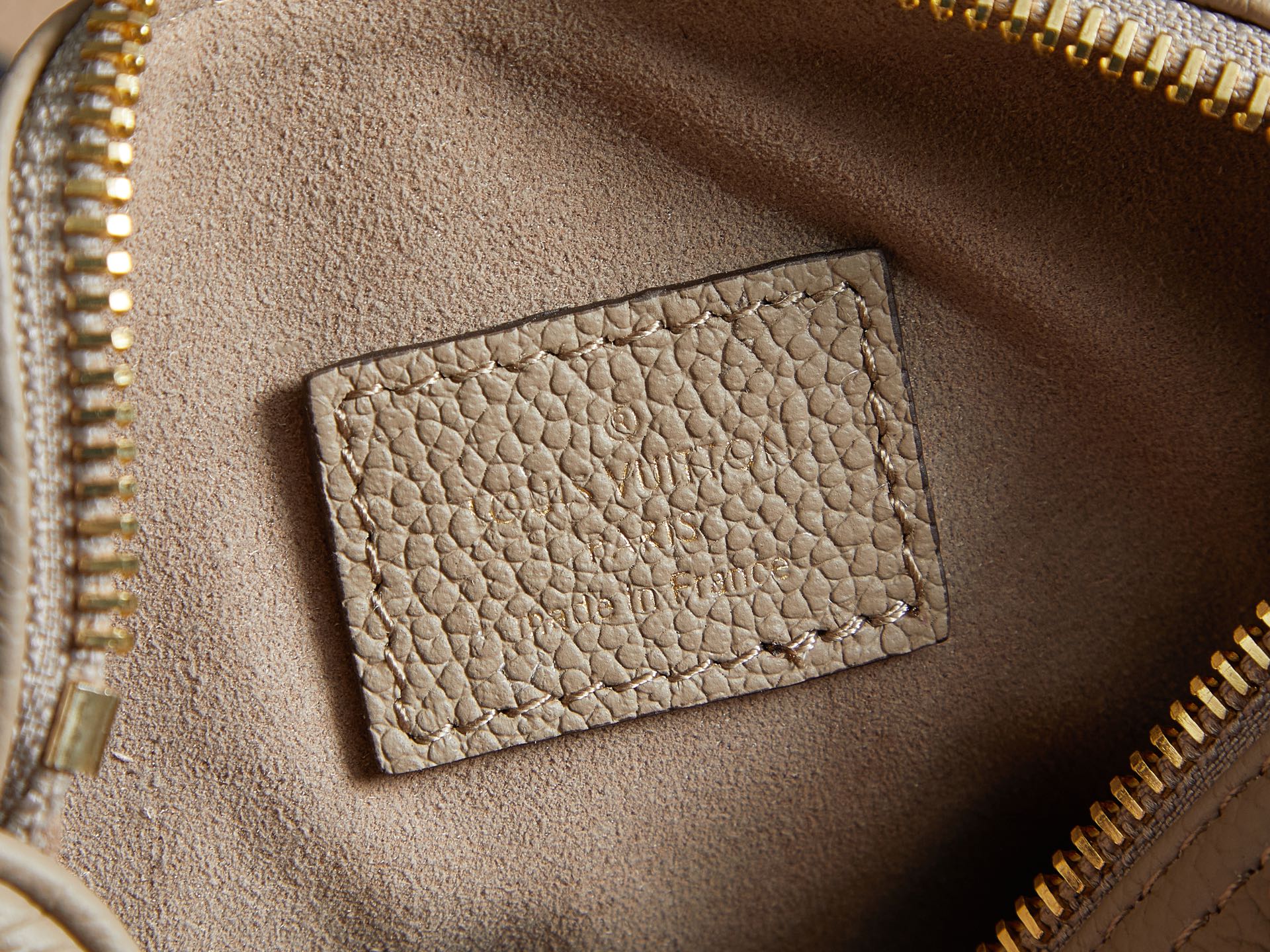 Louis Vuitton monogram handbag interior close-up: beige pocket panel with gold zipper teeth