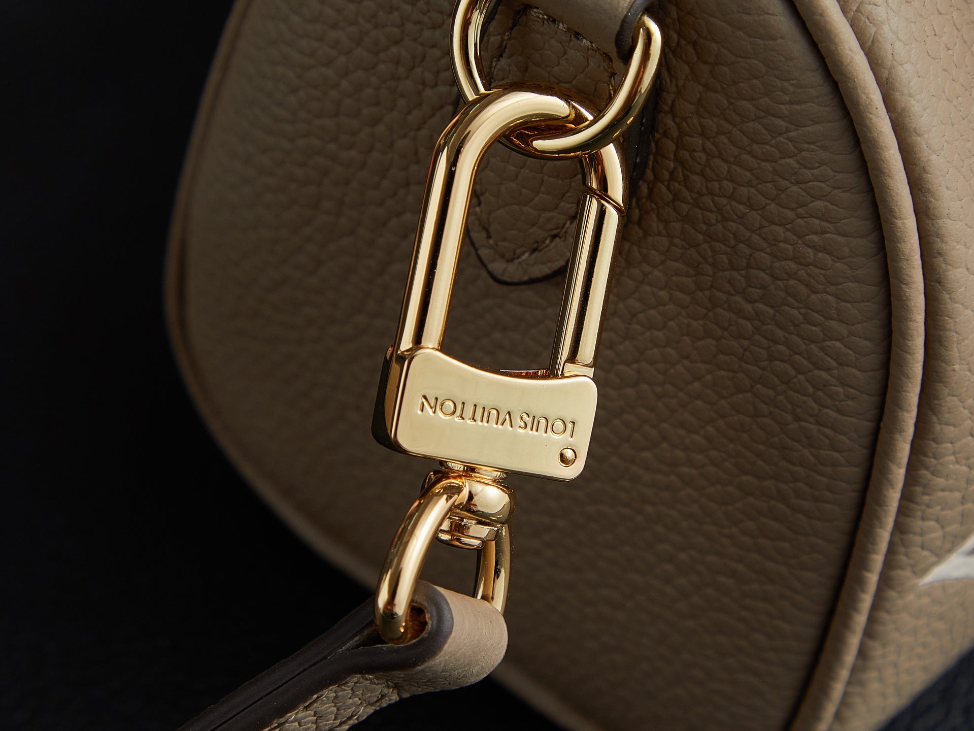 Louis Vuitton monogram handbag clasp close-up: gold padlock lock hardware on beige leather