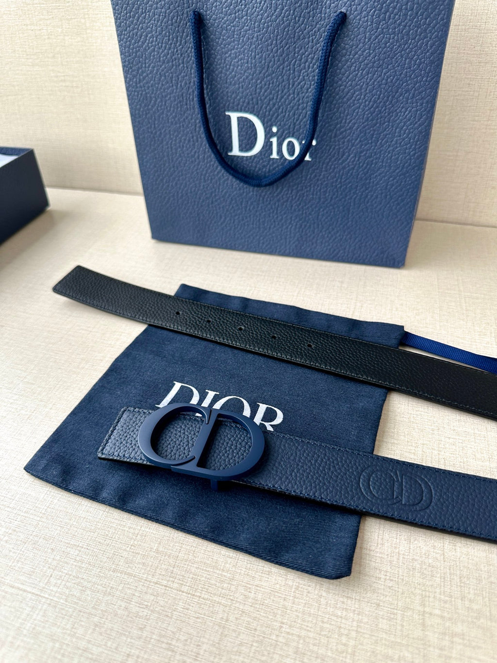 Blue leather Dior belt with CD buckle, laid beside Dior logo insert