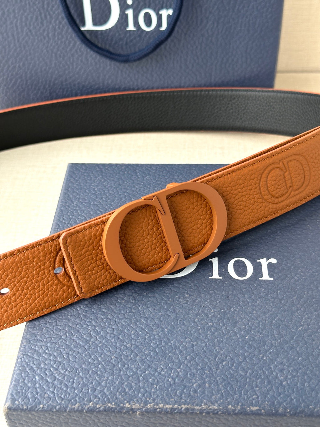 Tan leather belt with oval CD buckle and embossed logo pattern on strap