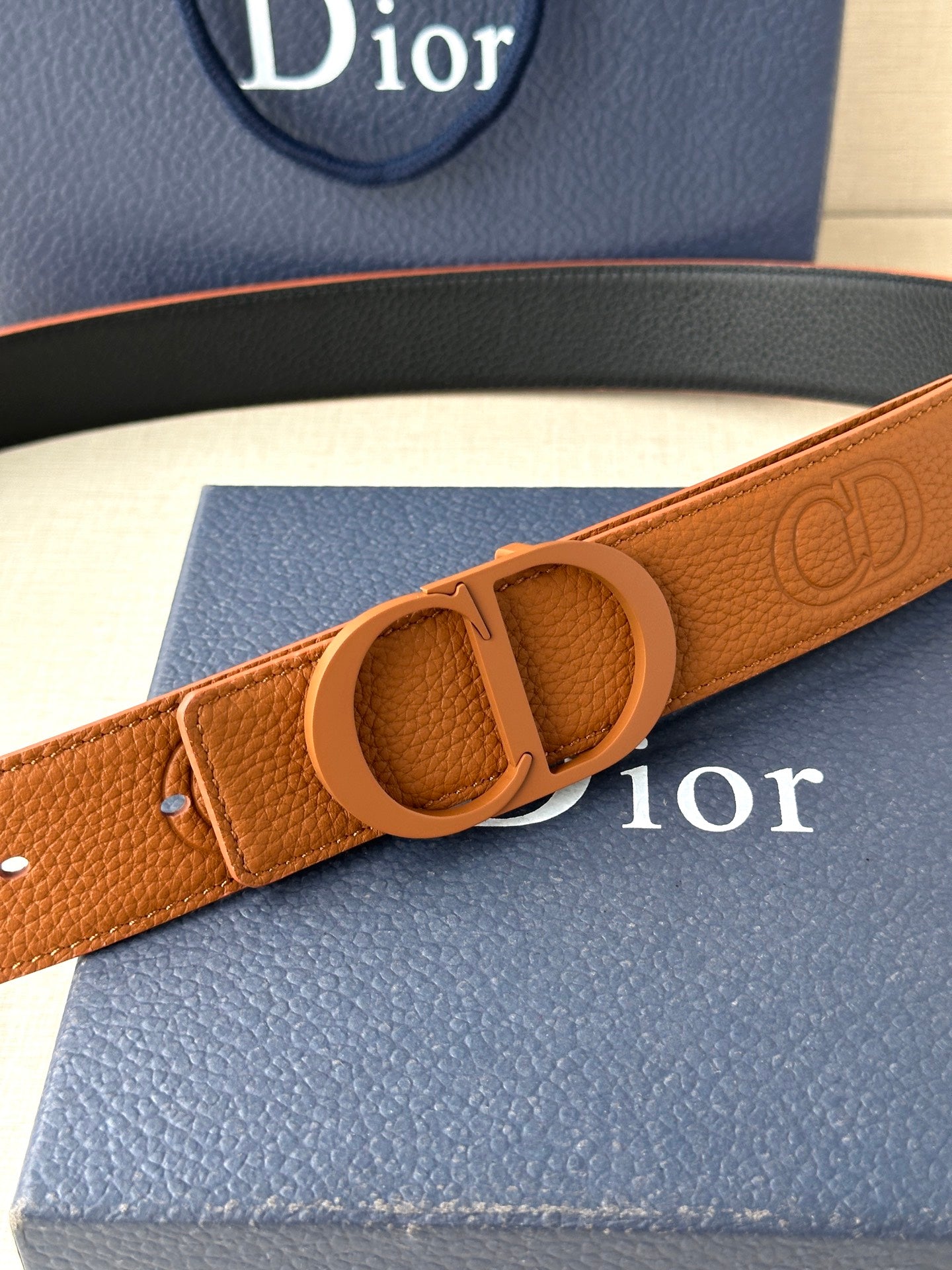 Tan leather belt with oval CD buckle and embossed logo pattern on strap
