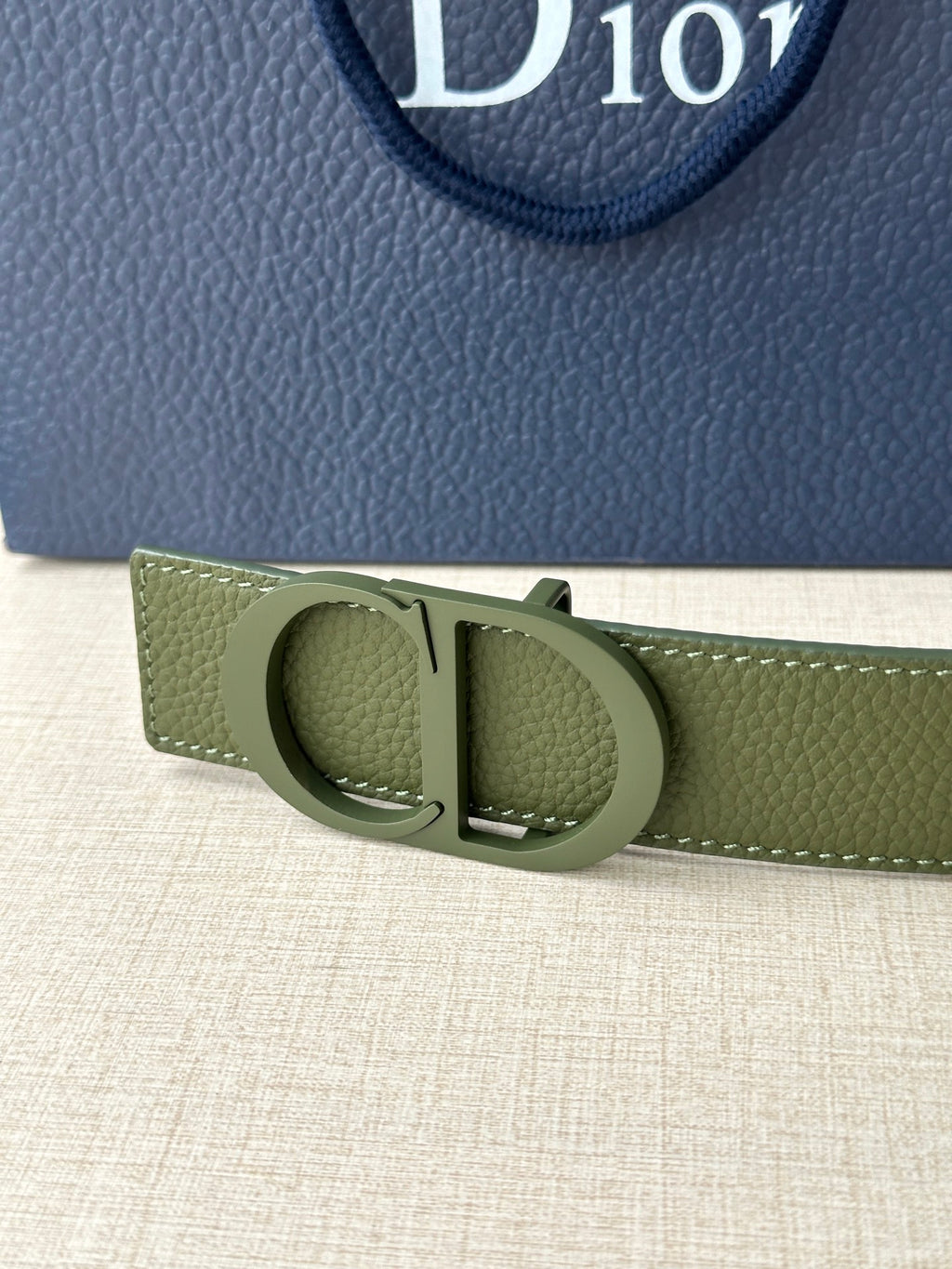 Dior belt buckle close-up in olive green leather with circular clasp and metal bar