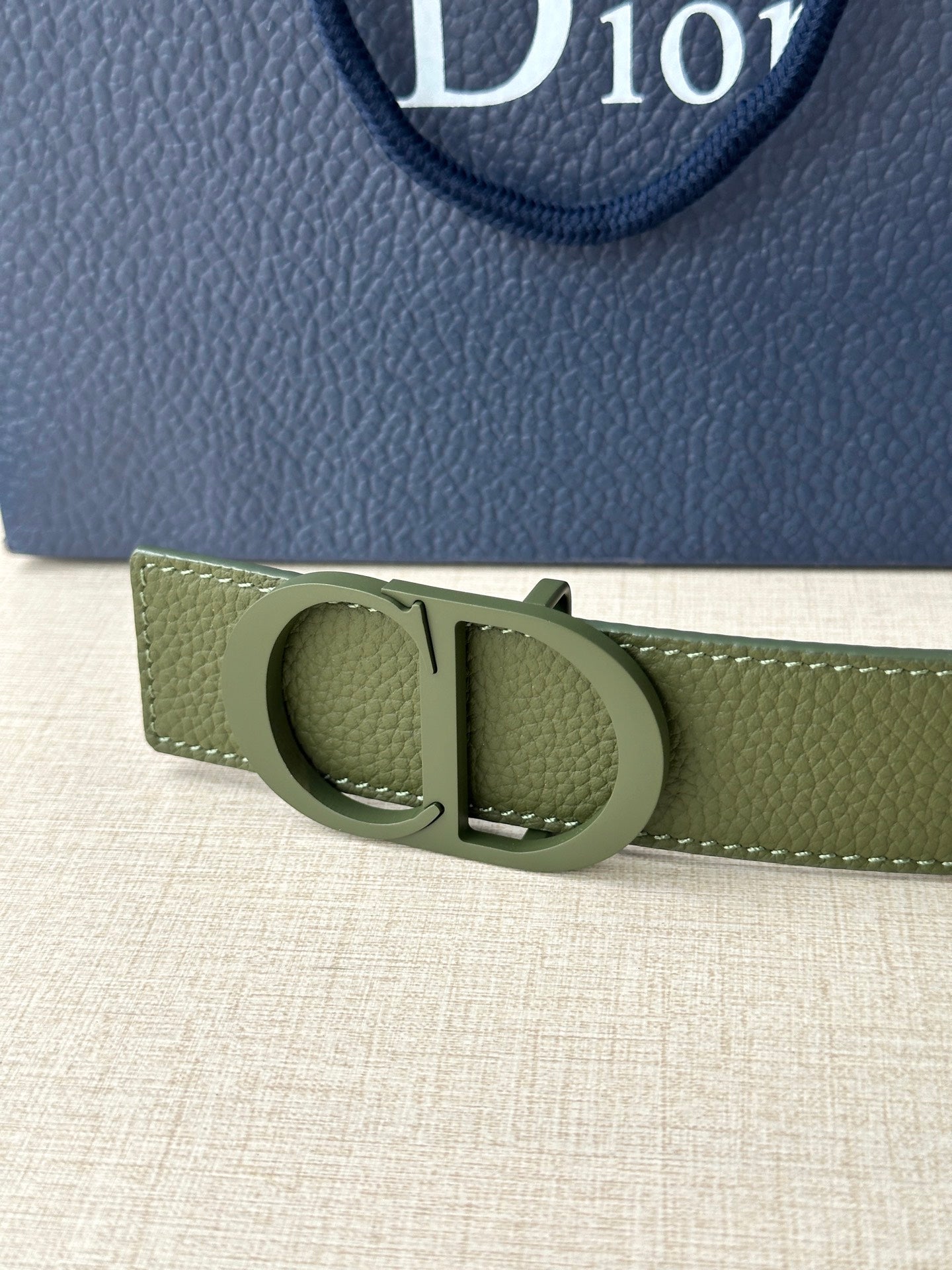 Dior belt buckle close-up in olive green leather with circular clasp and metal bar