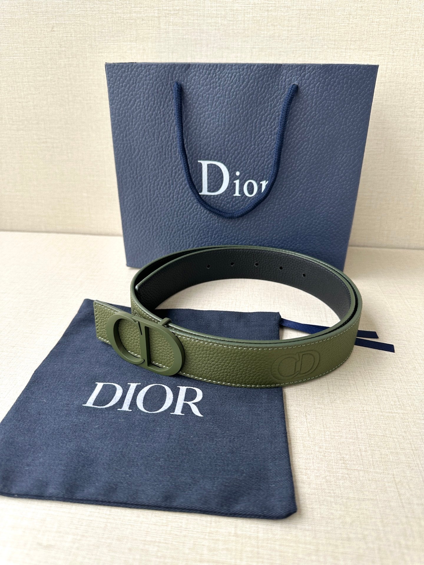Dior belt with olive green leather strap and round logo buckle, flat lay