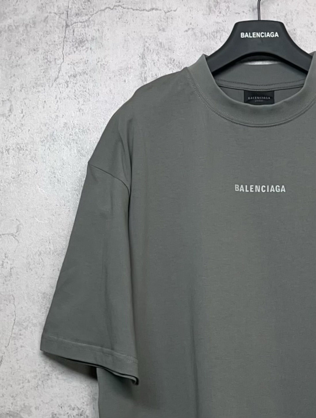 Balenciaga short-sleeve T-shirt on hanger, dark gray-green with small chest logo.