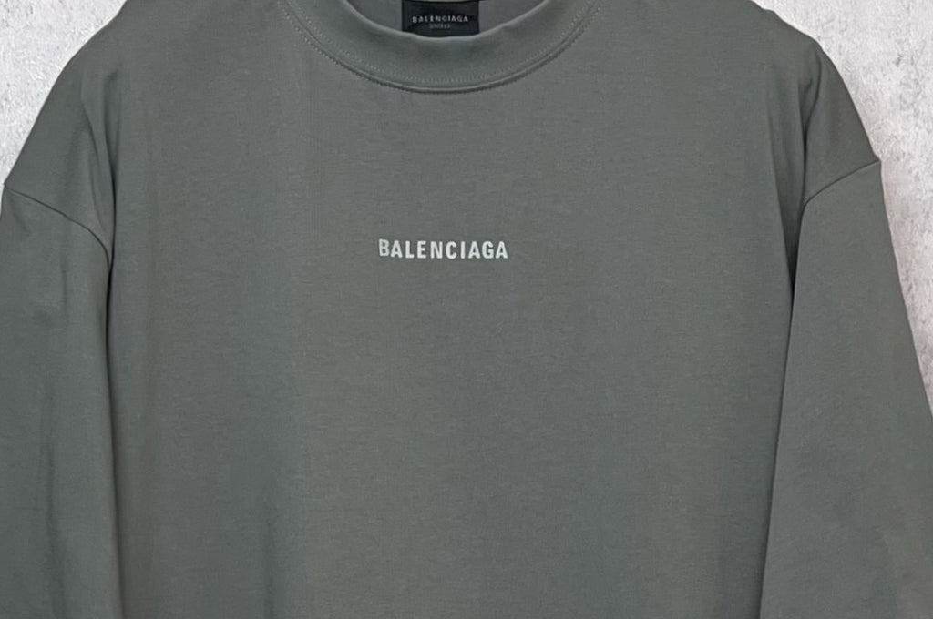 Balenciaga short-sleeve T-shirt close-up, dark gray-green crew neck and chest logo.