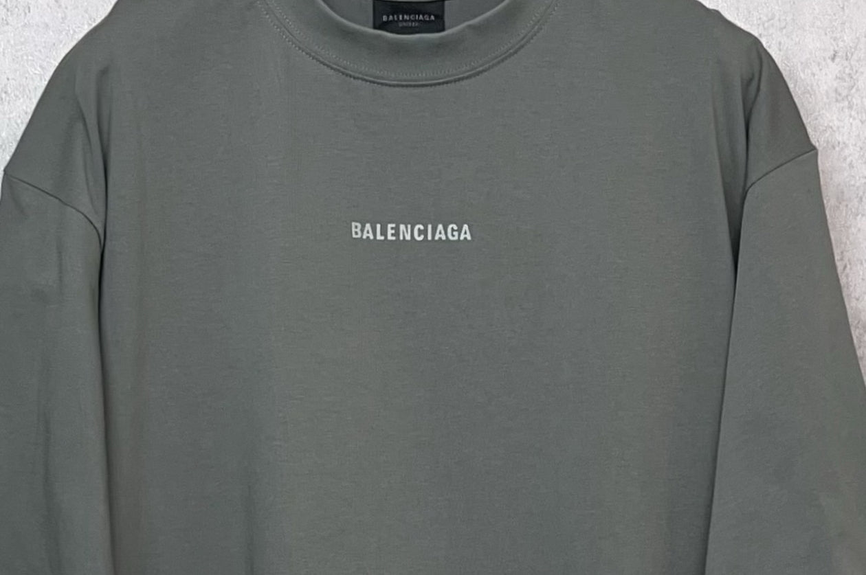 Balenciaga short-sleeve T-shirt close-up, dark gray-green crew neck and chest logo.