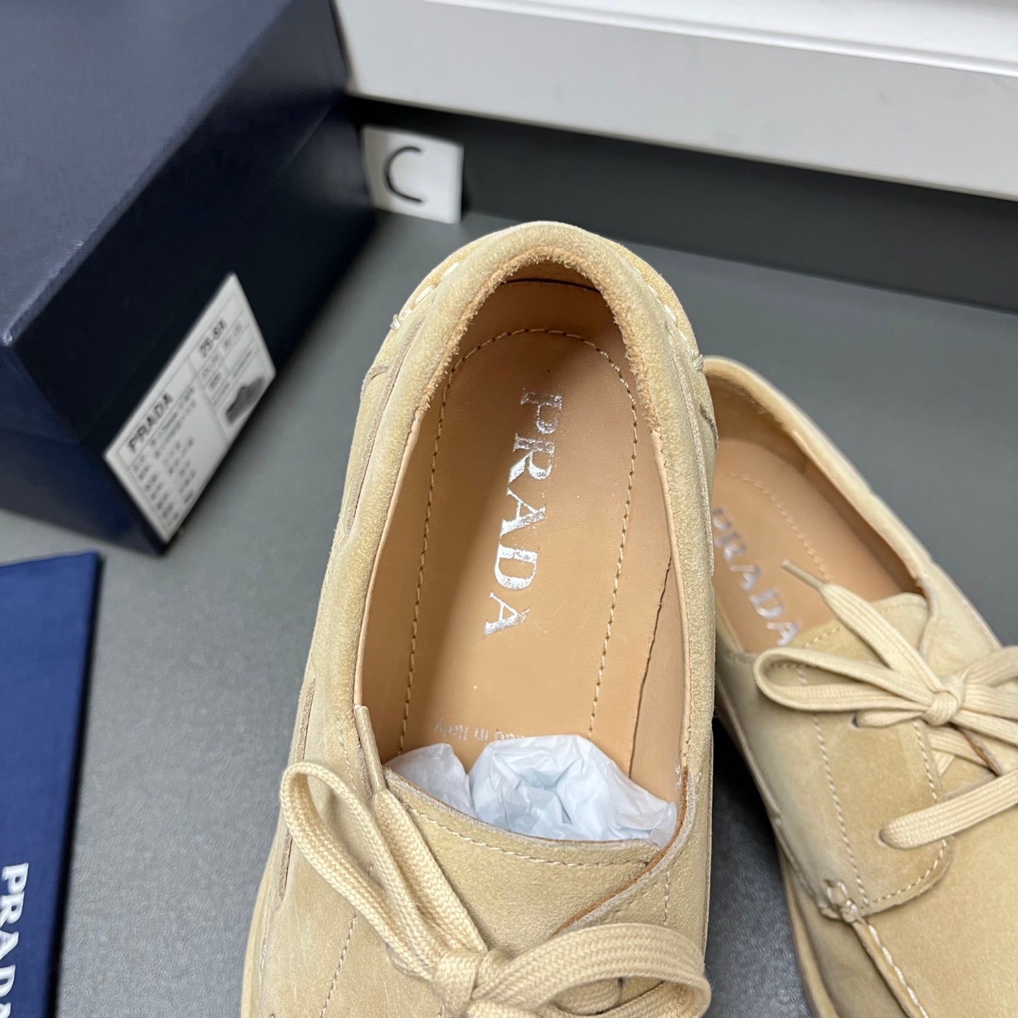 Beige suede lace-up loafers with open tongue showing Prada logo on insole