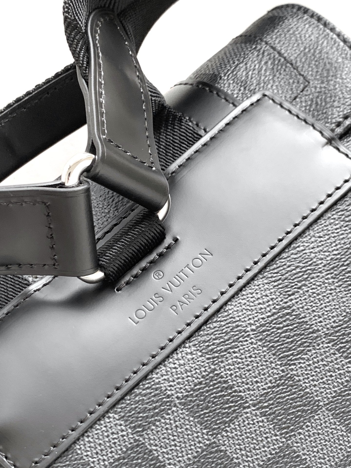 Men's Louis Vuitton checkered bag close-up with leather tab and stitched logo label