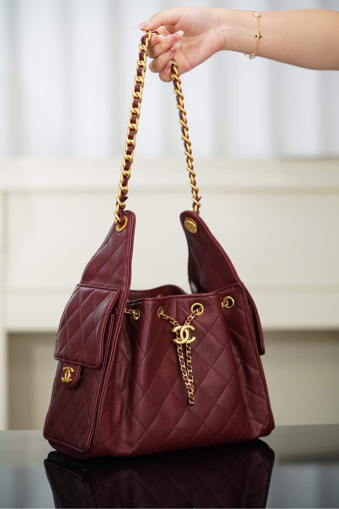 Chanel quilted shoulder bag in dark red held by gold chain strap; CC logo at front