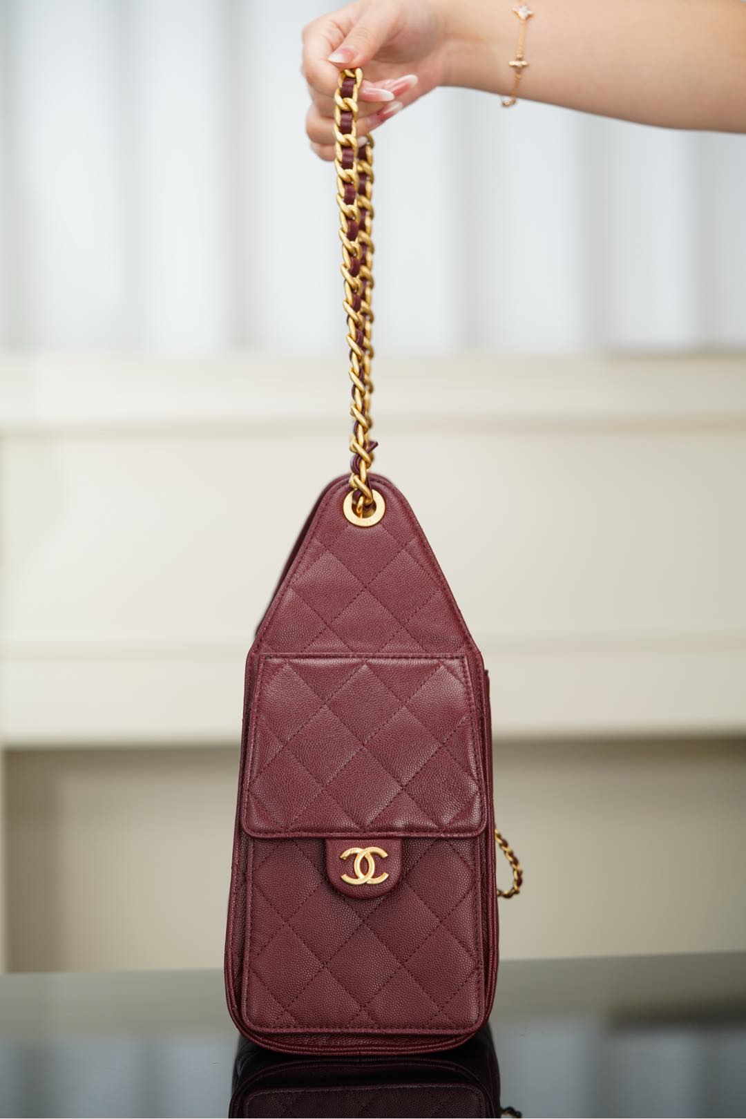 Chanel quilted bag in dark red hanging by gold chain strap with CC logo front patch