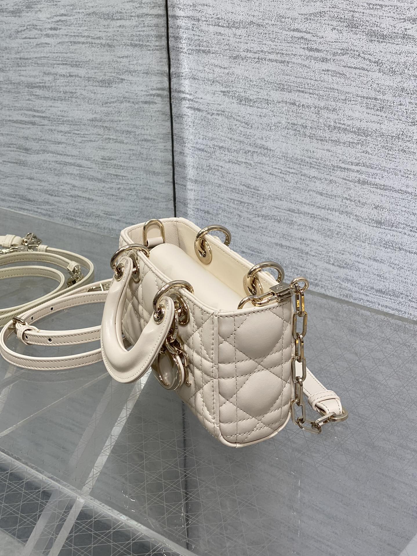Cream quilted Dior bag with short top handle, crossbody strap, and gold hardware