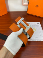Orange leather belt with black underside and silver studded H buckle close-up