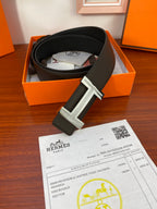 Black belt in box with silver-toned buckle and receipt card on wood surface