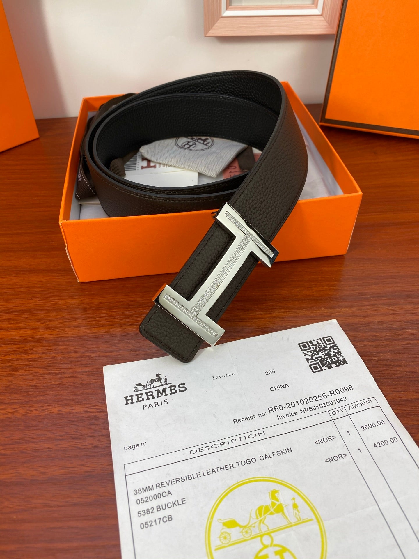 Black belt in box with silver-toned buckle and receipt card on wood surface