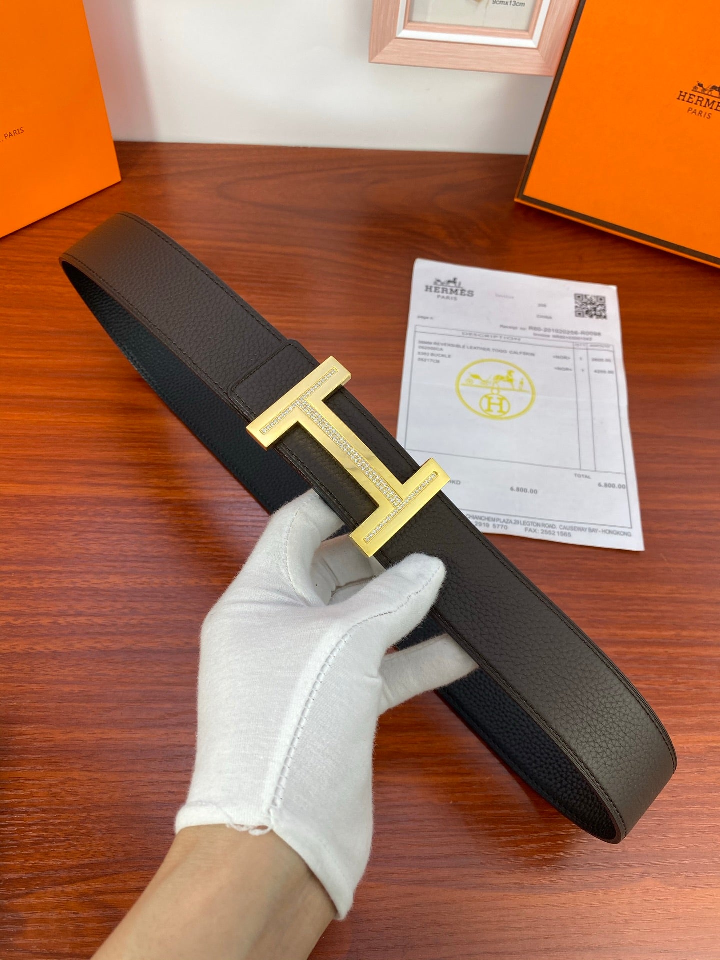 Hermes belt with black textured strap and gold-tone H buckle, with receipt card