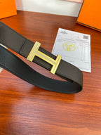 Black textured belt with gold-tone H buckle, laid flat with paperwork nearby