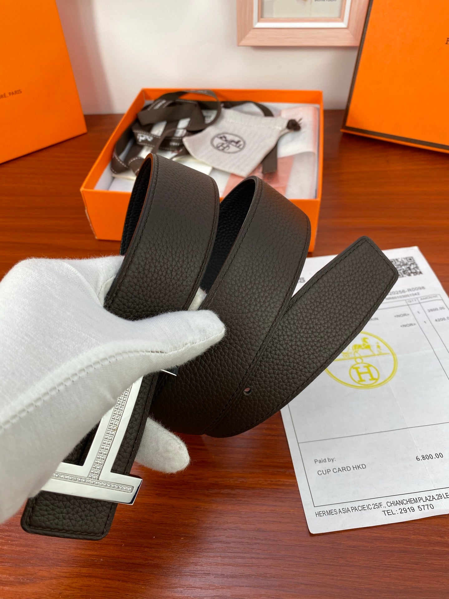 Black textured belt in gift box with silver-toned buckle, white gloves holding strap