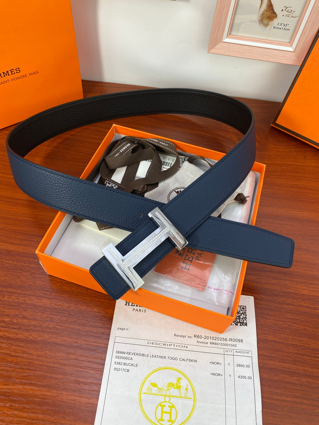 Dark blue leather belt with gold-toned buckle inside a box, styled on top view.