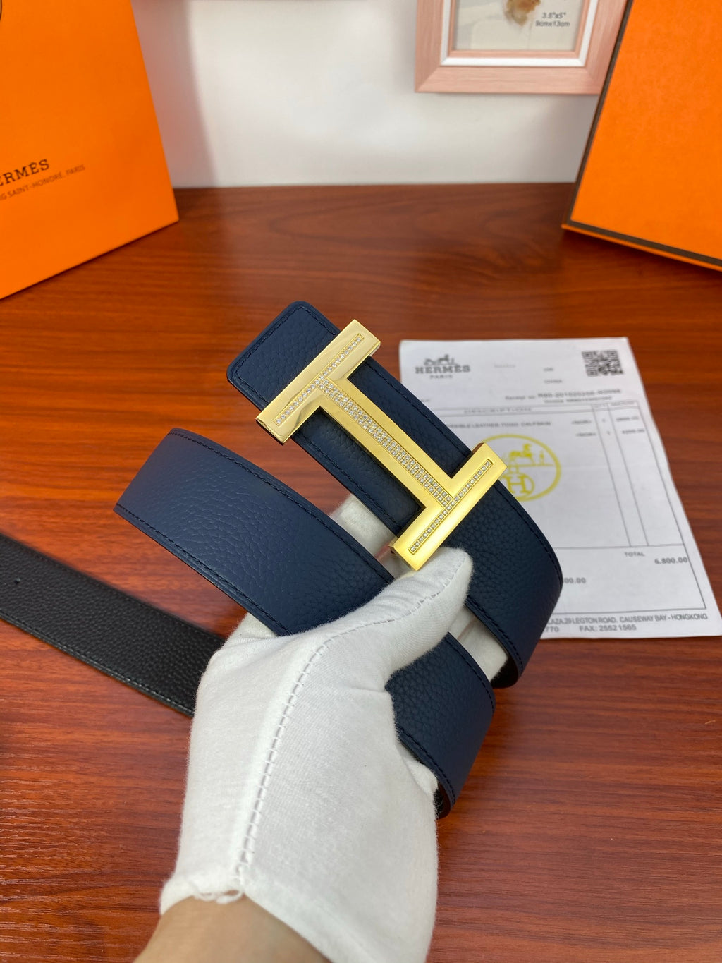 Dark blue leather belt with gold buckle, with packaging papers beneath the belt.