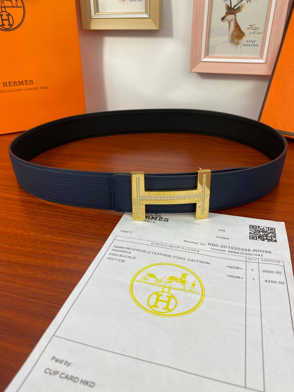 Dark blue leather belt with gold buckle, shown looped with paperwork placed underneath.