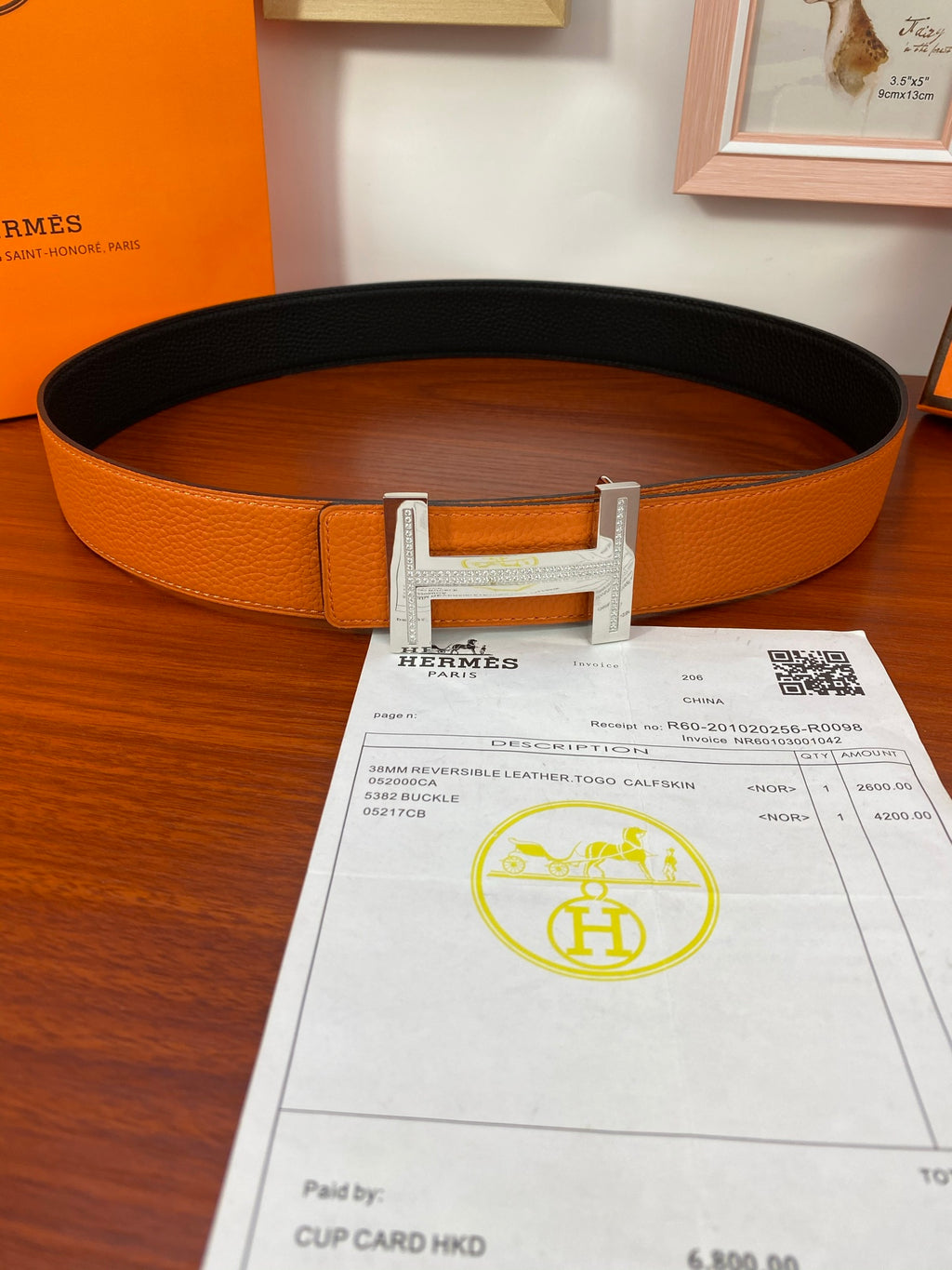 Reversible leather belt, orange leather with silver-tone H buckle, top view.